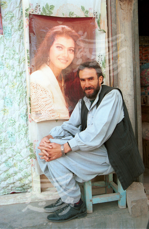 Man in Herat, Afghanistan, sitting in front of the poster of a female film star